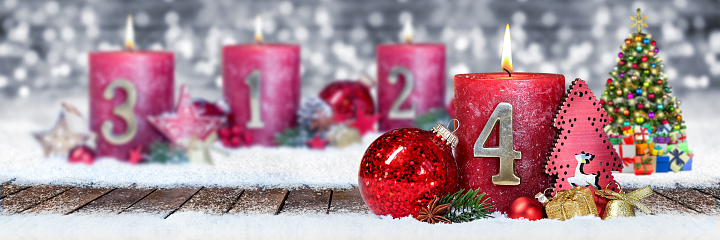 fourth sunday of advent red candle with golden metal number one on wooden planks in snow front of silver panorama bokeh background