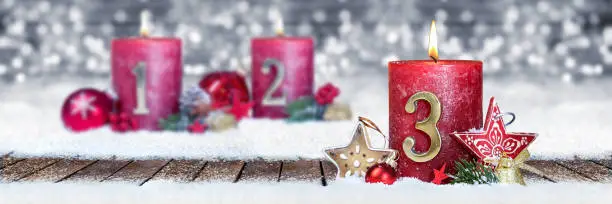 third sunday of advent red candle with golden metal number one on wooden planks in snow front of silver panorama bokeh background