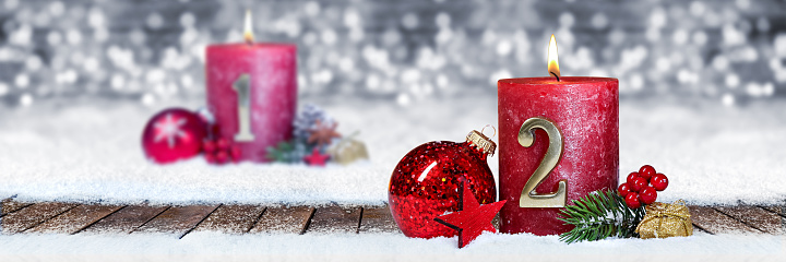 second sunday of advent red candle with golden metal number one on wooden planks in snow front of silver panorama bokeh background