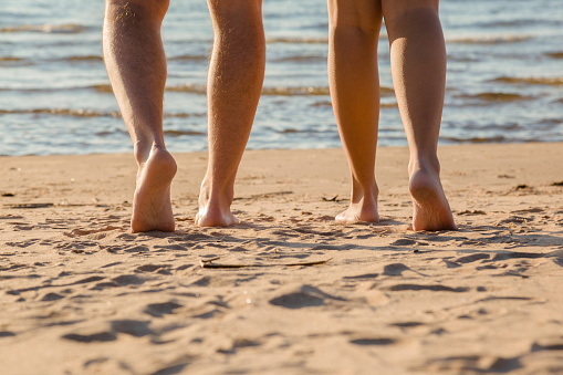 Young couple's barefoot going to swim in cold sunny day. Woman legs have goosebumps. Back view. Closeup.