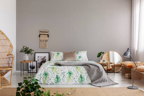 istock Real photo of double bed with leafy sheets placed in bright bedroom interior with macrame on the wall, mirror and posters on the floor and fresh plants 1068342488