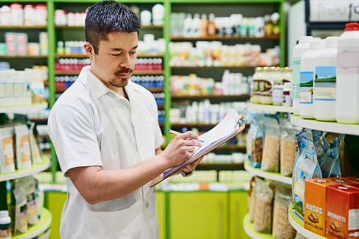 Shot of a confident man making notes on a clipboard while working in a health store
