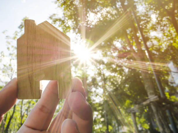 Hand holding wooden house with green forest background blurred and sun lighting Hand holding wooden house with green forest background blurred and sun lighting legacy concept photos stock pictures, royalty-free photos & images