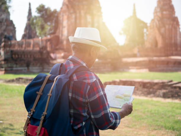 istock Senior man Asian with backpack look searching direction on location map at Wat Chaiwatthanaram. Ancient and historical attractions of Ayutthaya province thailand. Travel, Tourist Concept 1068350306