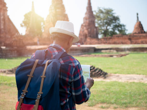 istock Senior man Asian with backpack look searching direction on location map at Wat Chaiwatthanaram. Ancient and historical attractions of Ayutthaya province thailand. Travel, Tourist Concept 1068350316