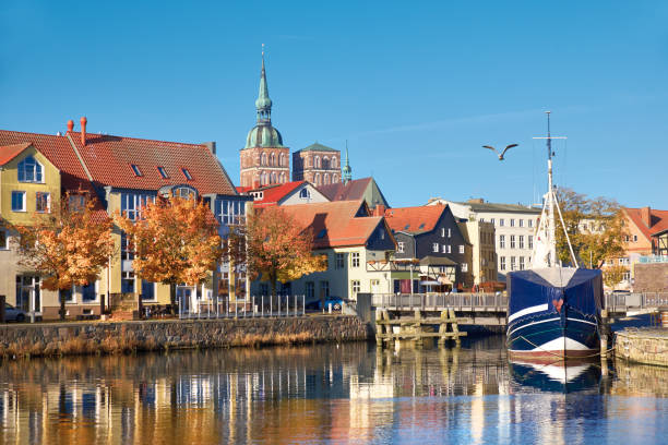 Docked sail boats and houses reflecting in channel with brick towers of Stralsund, Germany stock photo