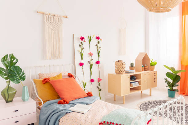 istock Handmade macrame above single feminine bed with pillows and patterned duvet, real photo of stylish bedroom with wooden furniture and flower board 1068354218
