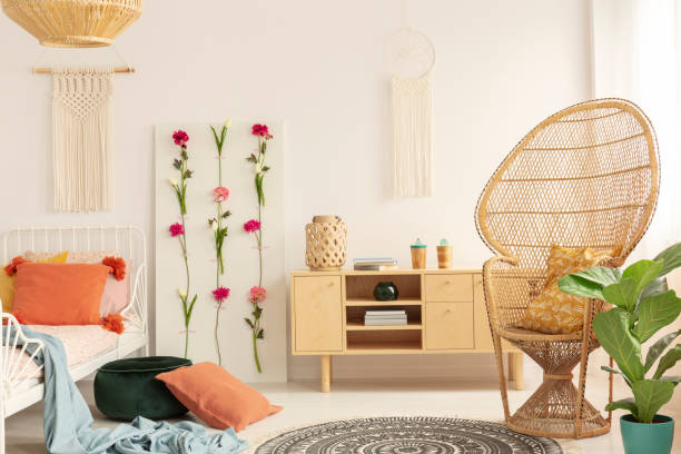 istock Wicker peacock chair with patterned pillow in cozy bedroom interior with macrame on the wall, flower board and wooden cabinet, real photo 1068354224