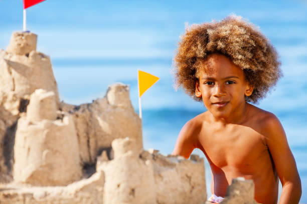 Close-up portrait of African boy building sandcastle on the beach in summer