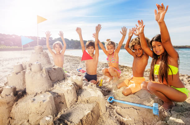 istock Happy friends sitting on beach around sandcastle 1068362892