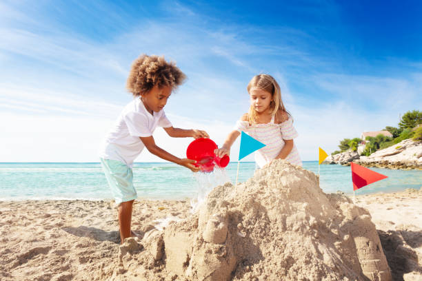 Cute boy and girl building sandcastle on the beach Happy boy and girl pouring water from bucket, building sand castle on the beach sand castle stock pictures, royalty-free photos & images