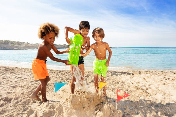 Two young siblings pay together in the sand during a family camping trip.  They are both dressed comfortably and are focused on building a sandcastle together.