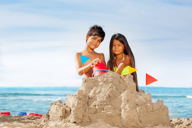 A happy couple enjoys a sunny beach day, building sandcastles while holding a teddy bear affectionately