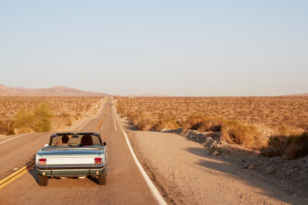 istock Couple driving convertible car on desert highway, back view 1068365782