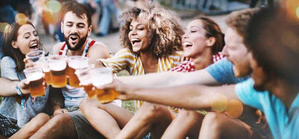 Let's have some beers. Closeup of group of young adults having some beers while hanging out on a summer afternoon. One of them is partially visible but released. beer festival photos stock pictures, royalty-free photos & images