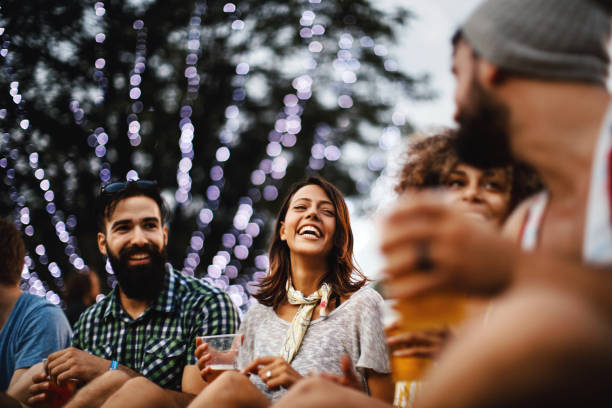 Friends having some beers at a concert. Closeup of group of young adults sitting on the ground and having some beers and laughing on a summer afternoon. Some of them are obscured but released. beer festival photos stock pictures, royalty-free photos & images