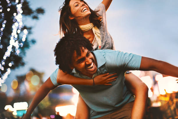 Let's party. Closeup low angle view of a young multi ethnic couple enjoying a concert. He's piggybacking her, blurry stage in background. festival goer stock pictures, royalty-free photos & images