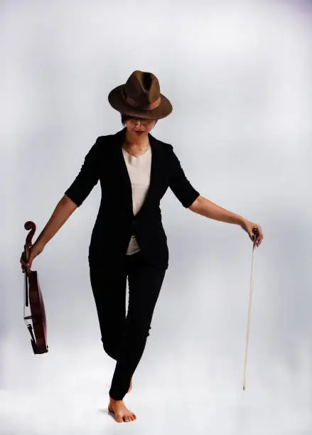 The lady is wearing black suit and brown hat,stand on stage and hold violin and bow in hand,prepare for playing