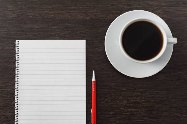 istock Notebook with pen and cup of coffee on brown wooden table 1068389808
