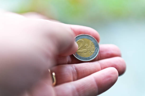 A senior man's hand holding a two Euro coin.