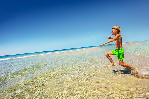 Side view portrait of happy boy running in shallow sea water