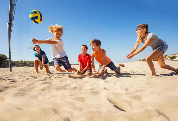 Portrait of happy teenage boy making bump pass during beach volleyball game with friends