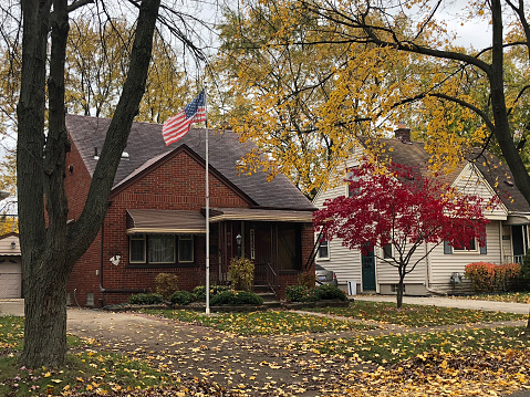 Dearborn, Michigan-November 8, 2018:  Typical 1950's suburban home in the autumn with colored leaves on the tree and covering the grass.  An American flag waves in the breeze.