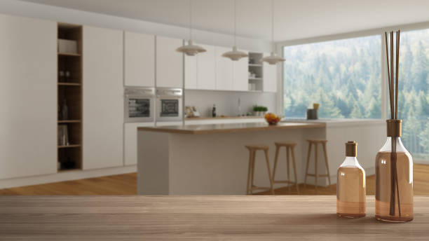 istock Wooden table top or shelf with aromatic sticks bottles over blurred modern minimalist white and wooden kitchen with island and big panoramic window, white architecture interior design 1068438366
