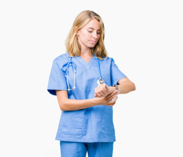 belle jeune médecin femme portant des uniformes médicaux sur fond isolé regarder l’heure sur une montre bracelet, détendu et confiant - checking the time watch women looking photos et images de collection