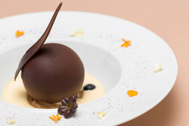 istock Luxurious dessert with chocolate globe and vanilla sauce,  served on a biscuit,  decorated with chocolate flower,  flower petals and forest fruits,  served in a white plate,  light background,  isolated 1068443690