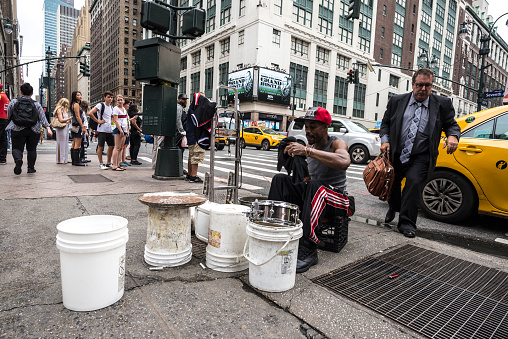 New York City, USA - July 25, 2018: Drummer man playing from plastic pots like a drum on Seventh Avenue (7th Avenue) while a man in a suit comes out of a taxi and people around in Manhattan in New York City, USA