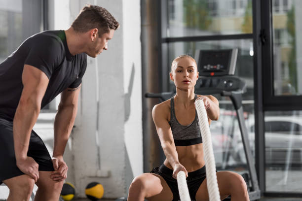 istock attractive athletic bodybuilder working out with ropes in gym, trainer looking at her 1068447594