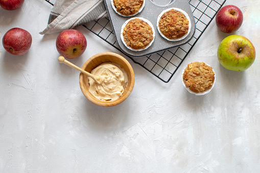 Homemade baking - flat lay of fresh baked apple muffins on cooling rack, organic apples, spiced butter in wooden bowl, white background, top view, copy space.