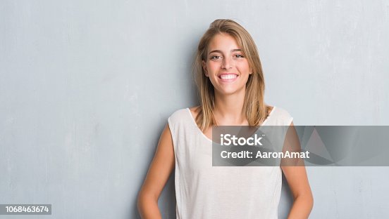 istock Beautiful young woman standing over grunge grey wall with a happy face standing and smiling with a confident smile showing teeth 1068463674