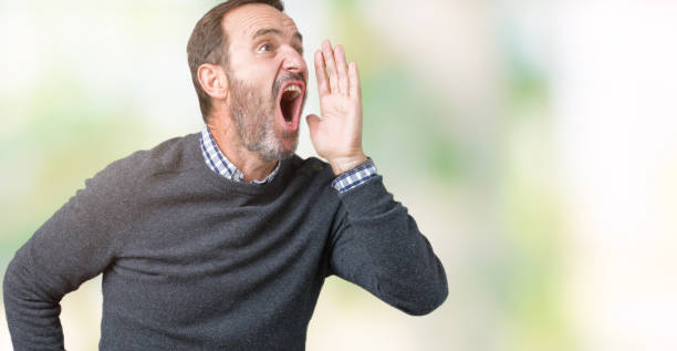 istock Handsome middle age senior man wearing a sweater over isolated background shouting and screaming loud to side with hand on mouth. Communication concept. 1068467994