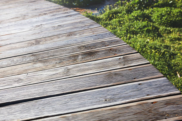 Vintage brown wooden planks of a curved boardwalk over the green fields. Close up view