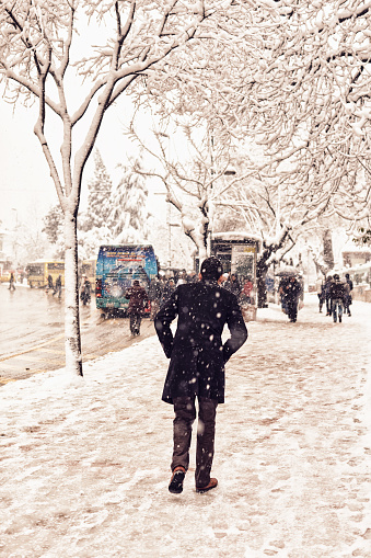 Scenes from everyday street life in Turkey. People walking on a snow covered sidewalk in stormy weather with traffic at the background