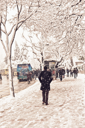 Scenes from everyday street life in Turkey. People walking on a snow covered sidewalk in stormy weather with traffic at the background