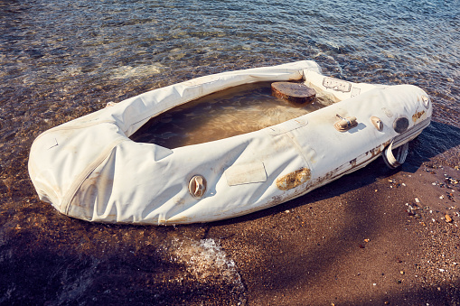 Old white inflatable flat boat washed up on the shore