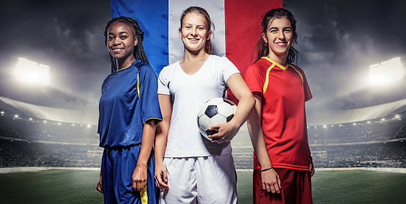 Three mixed race Female Football Players with a Soccer Ball in front of Stadium Lights and a french flag