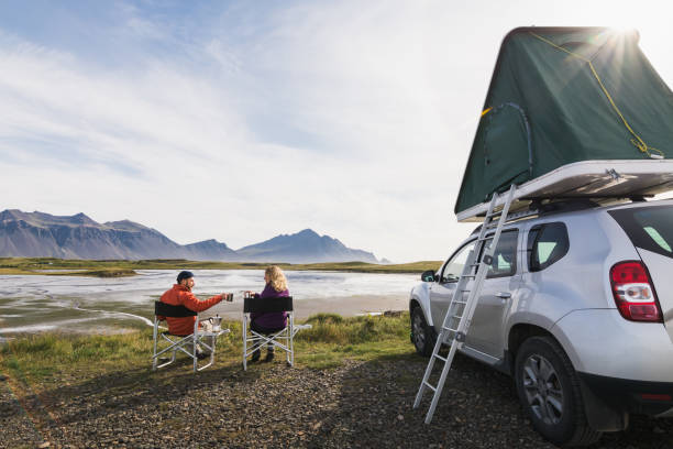 Young couple sitting in folding chairs next to offroad car with tent on the roof stock photo
