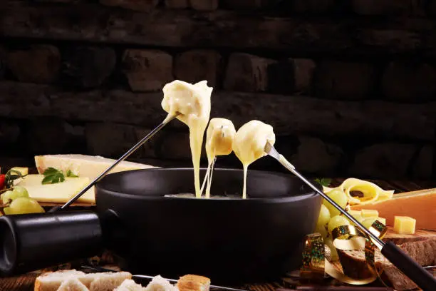 Gourmet Swiss fondue dinner on a winter evening with assorted cheeses on a board alongside a heated pot of cheese fondue with two forks dipping bread in a tavern or restaurant