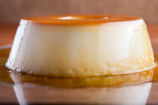 scene composed of a milk pudding with caramel syrup dripping up the wooden table