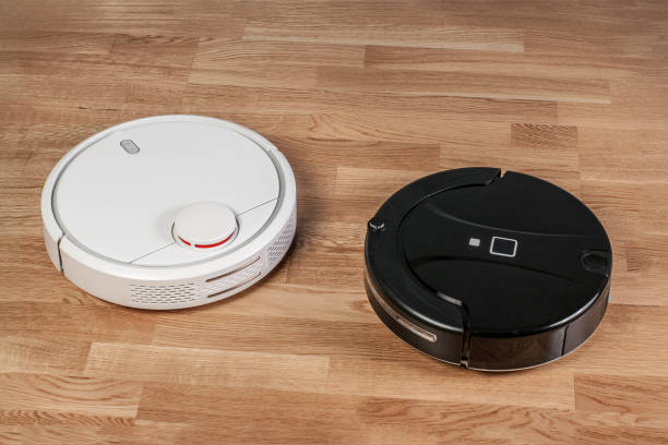 istock Two different robotic vacuum cleaners models cleaning dust on laminate floors. Modern smart cleaning technology housekeeping. Close up. Problem of choosing concept 1068560520