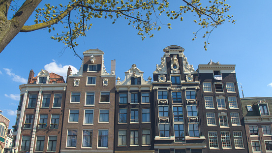 CLOSE UP: Gorgeous 17th century slim and high canal houses along Amsterdam waterway opened as museums, offices and hotels. Famous buildings with historic facades, skinny profile and grand gables