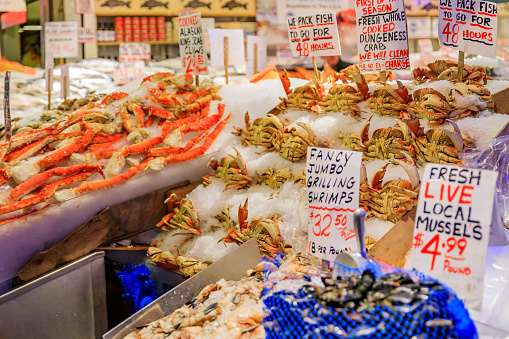 Fishmonger at a stall with fresh seafood like crab, shrimp and mussels for sale at Pike Place Market in Seattle, Washington