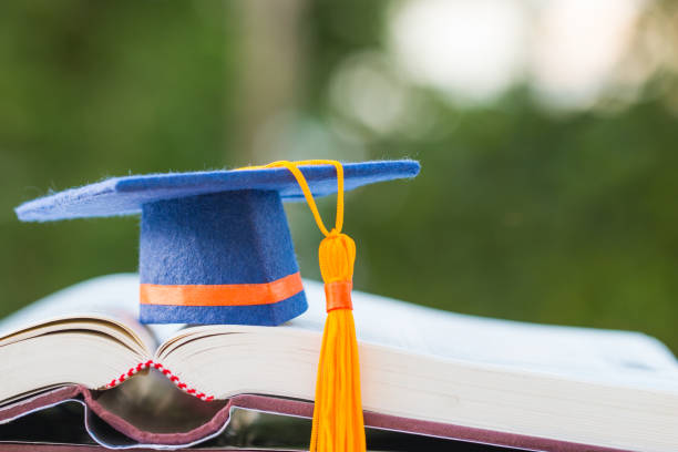istock Graduate or Education knowledge learning study abroad international concept : Blue Graduation cap on opening textbook with light green blur background at outside in campus, Back to School 1068584450