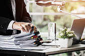 istock Businessman hands holding pen for working in Stacks of paper files searching information business report papers and piles of unfinished documents achieves on laptop computer desk in modern office 1068584492
