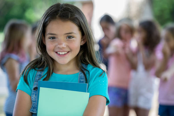 istock Happy little girl smiles while standing outside school with classmates 1068597320