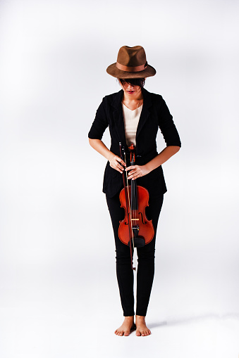 The lady is wearing black suit and brown hat,holding violin and bow in hand,standing on background,prepare for playing
